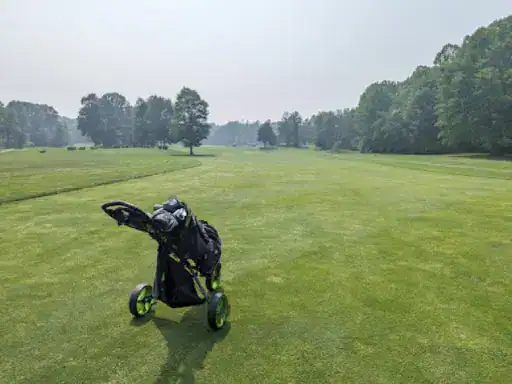 A golf cart with a bag sits on a quiet golf course, showing a peaceful day unlike the services J&P Coatings offers.