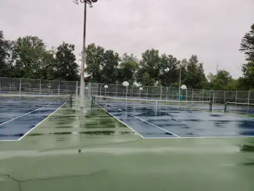 This image shows tennis courts that look slippery and unsafe because of water. J&P Coatings can help make these courts safer and stronger.