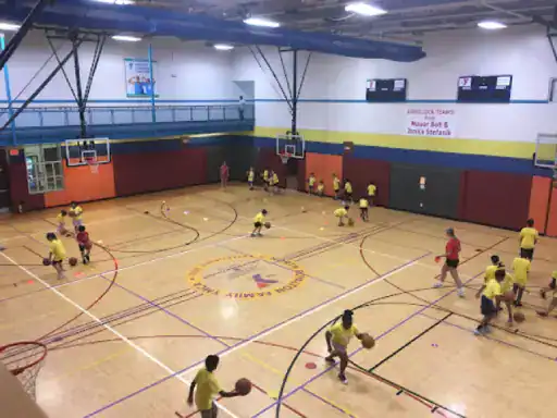 Kids and adults have fun learning basketball skills on a strong gym floor made by J&P Coatings. The scene shows active play thanks to the safe, lasting surface.