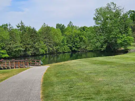 A peaceful pathway leads to a calm lake with a wooden bridge, showing how J&P Coatings can help create relaxing outdoor spaces.