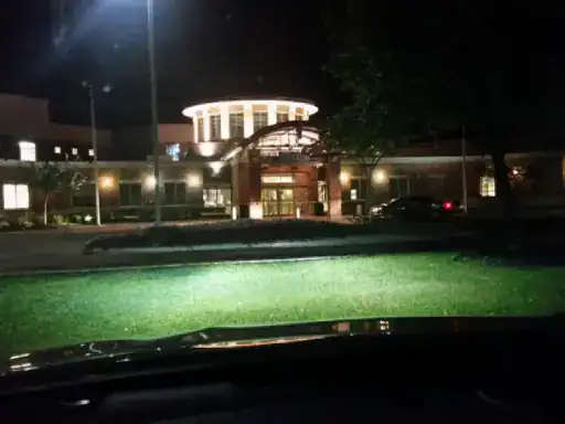 A photo showing J&P Coatings outside a building at night. Bright lights make the entrance and dome easy to see. The cars headlights help light up the grass in front.