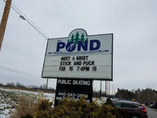 A sign at The Pond ice rink announces a Meet & Greet Stick and Puck event on February 15 from 7&ndash;8 PM for $5. J&P Coatings is shown as the sponsor. The sign also gives info about public skating and how to contact the rink. Alt text: Sign shows J&P Coatings sponsoring a $5 hockey event and sharing public skating details.