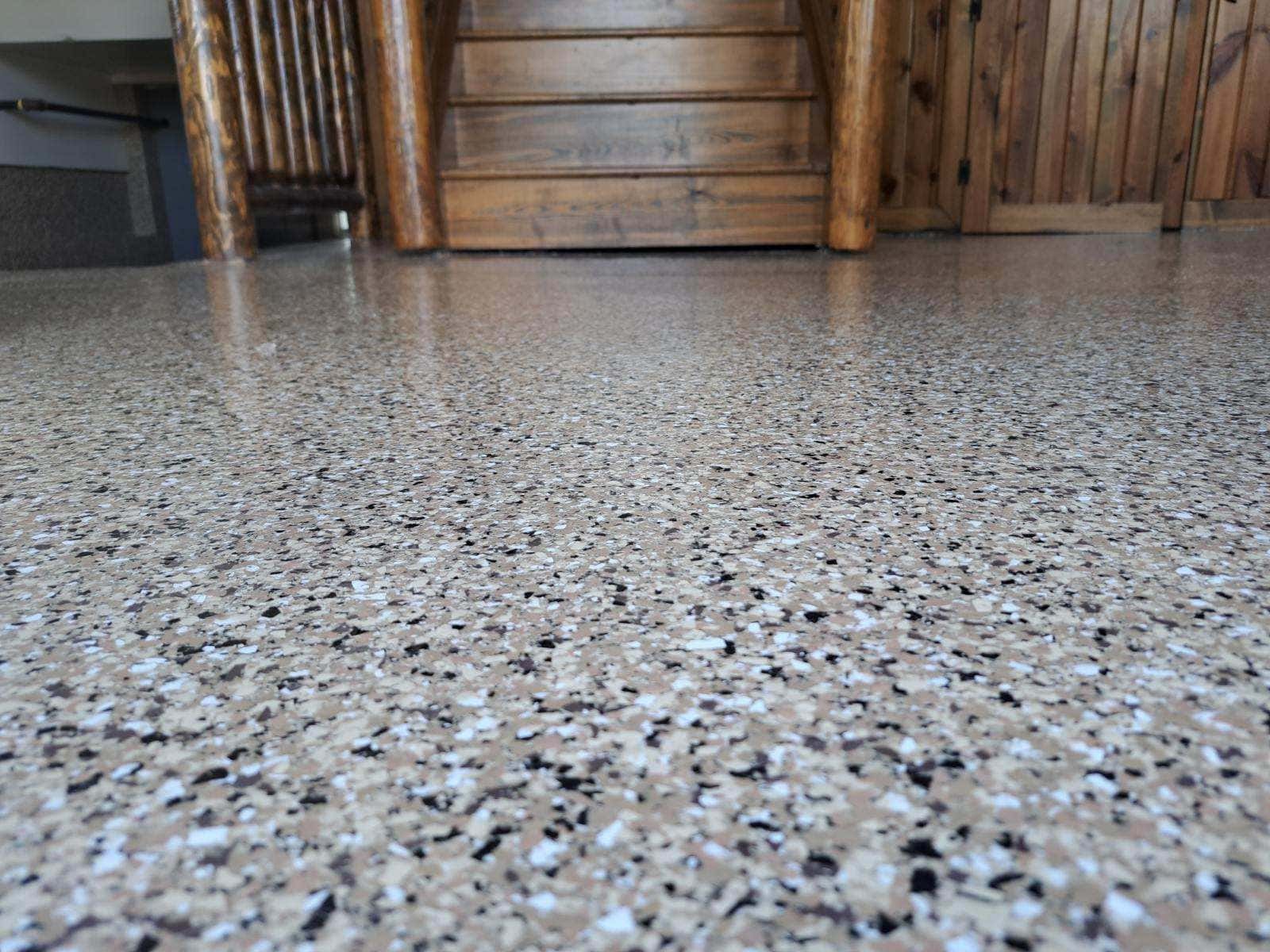 This image shows a smooth, speckled epoxy floor by J&P Coatings. It gives an idea of how your basement or patio can look after getting professional concrete coating. Wooden stairs hint that it works well indoors too.