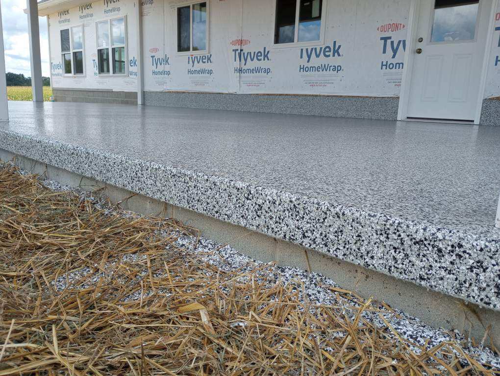 A new house, wrapped for construction, has a clean gray porch installed by J&P Coatings. The ground in front is covered with straw.