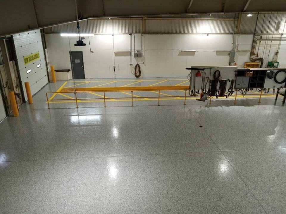 The photo shows a clean, spacious indoor area with polished floors coated by J&P Coatings. The area looks safe and organized for work, with safety features and utility equipment visible.