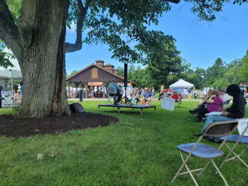 A guitar player performs on an outdoor stage while people relax and enjoy the event near a building improved by J&P Coatings.