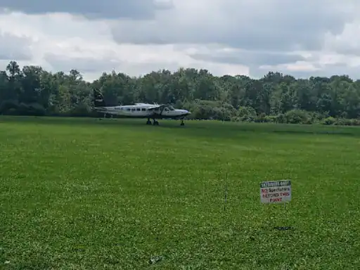 An airplane sits on grass near trees and clouds. A J&P Coatings sign says No Spectators Beyond This Point, showing the companys concrete coating expertise.
