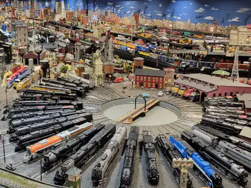 A model train display shows busy tracks and small buildings made by J&P Coatings, creating a lively city scene. Alt text: Model train display features city setting built by J&P Coatings.