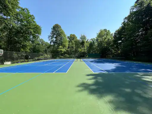 Two clean tennis courts by J&P Coatings show quality work. The courts are outdoors, surrounded by nature, and look ready for play.