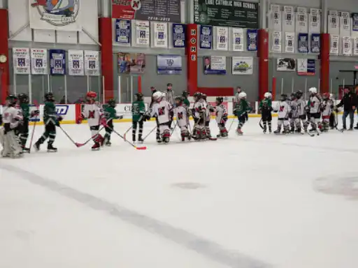 Youth hockey teams shake hands after a game with J&P Coatings ads for basement and patio coatings in the background.
