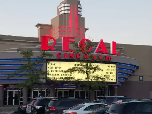 People are arriving at Regal Cinemas 16, where a movie list is shown above the entrance. The parking lot features work by J&P Coatings, known for their concrete patio coatings.