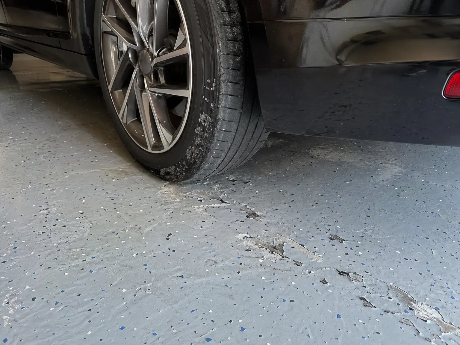 A black car’s tire on a cracked garage floor shows why J&P Coatings can help repair and protect damaged concrete surfaces.